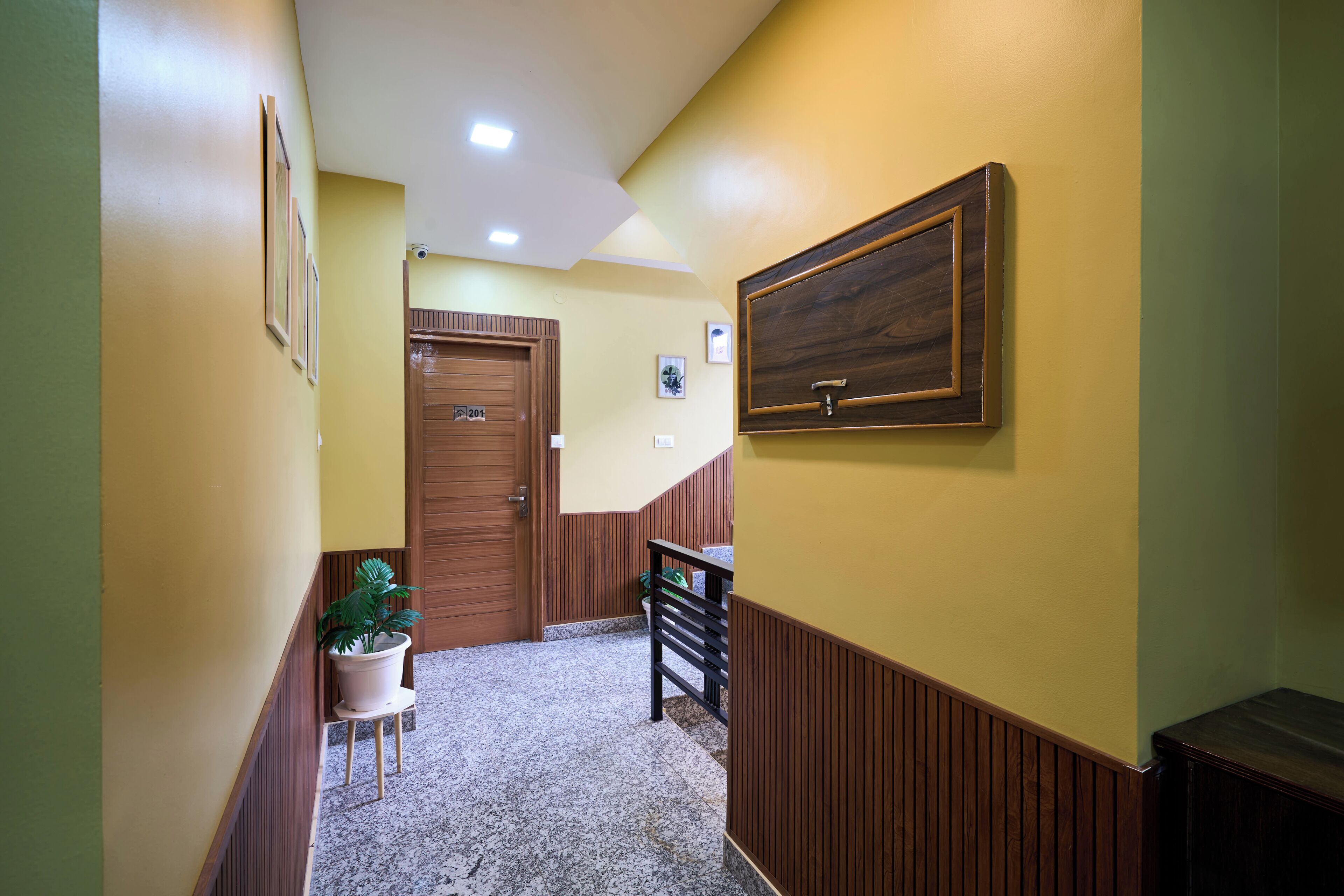 A hallway with a wooden door, a potted plant, a bench, and a framed picture on the wall.