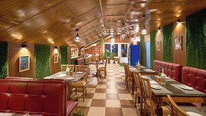 A restaurant with wooden ceilings, green wall accents, and red seating. Tables are set with plates and cutlery. - Treebo Roshan House With Valley View (Dharamshala)