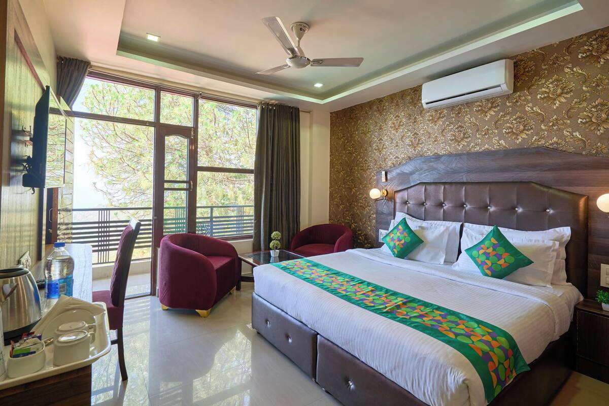 A bedroom with a large bed, a ceiling fan, an air conditioner, and a view of trees through the window.