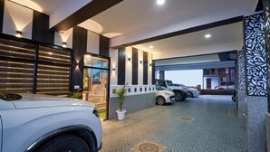 A modern hotel entrance with a reception desk, a parking area with several cars, and a decorative wall with a geometric pattern. - Treebo Roshan House With Valley View (Dharamshala)