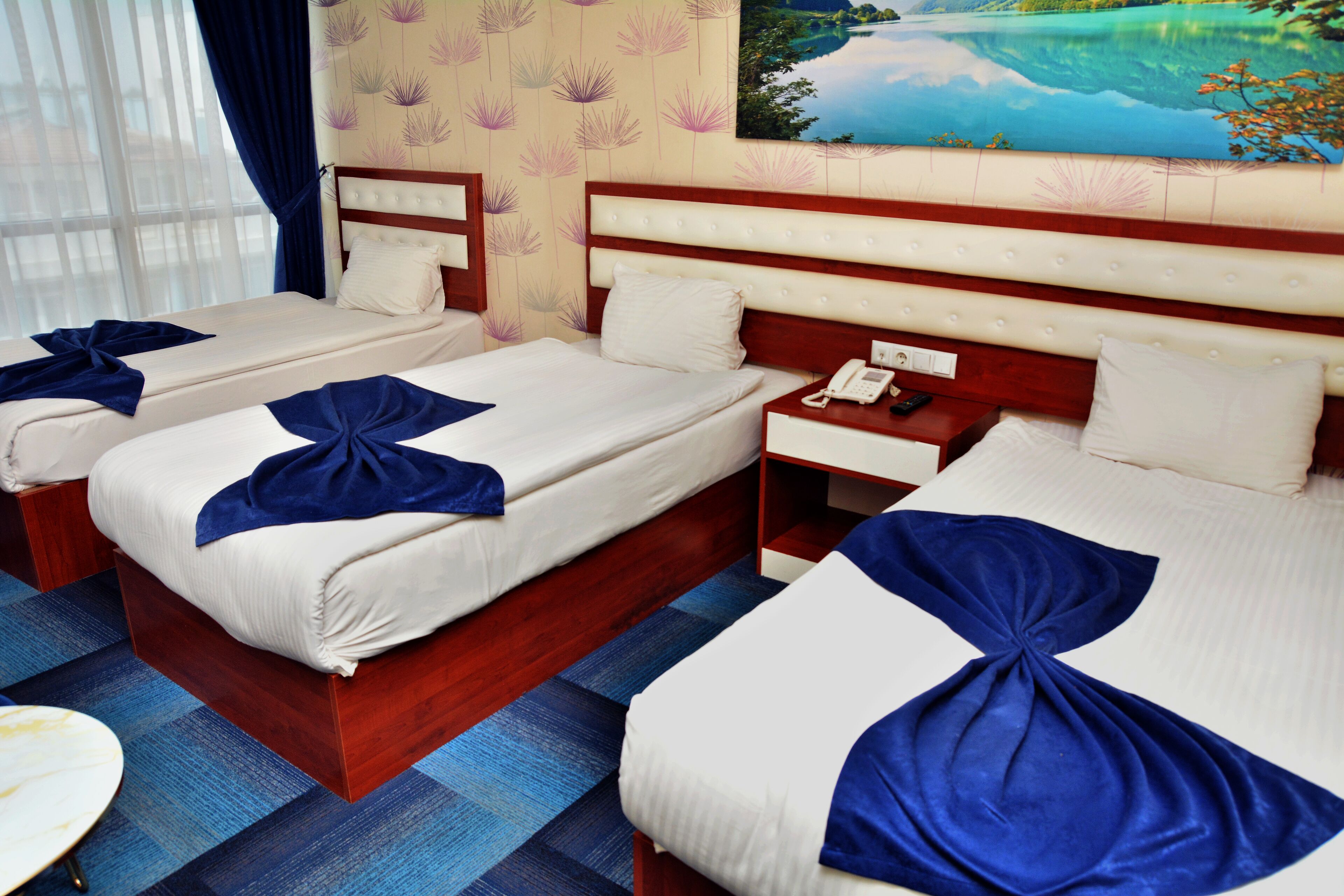 Una habitación de hotel con dos camas, cada una con una toalla azul. Se observa un mesita de noche con un teléfono y un cuadro en la pared.