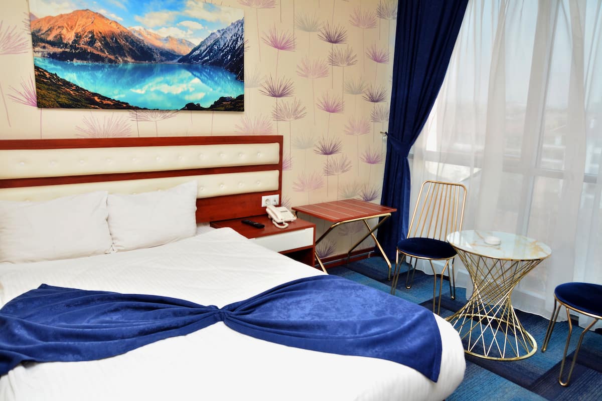 Quarto de hotel com cama, secretária, cadeira e vista para montanhas pela janela.