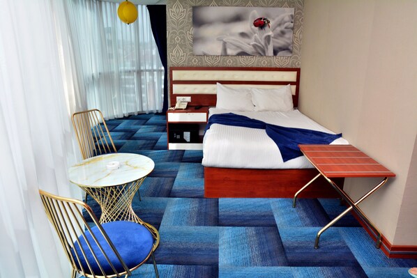 Una habitación de hotel con cama, mesita de noche, silla y una pequeña mesa con otra silla.