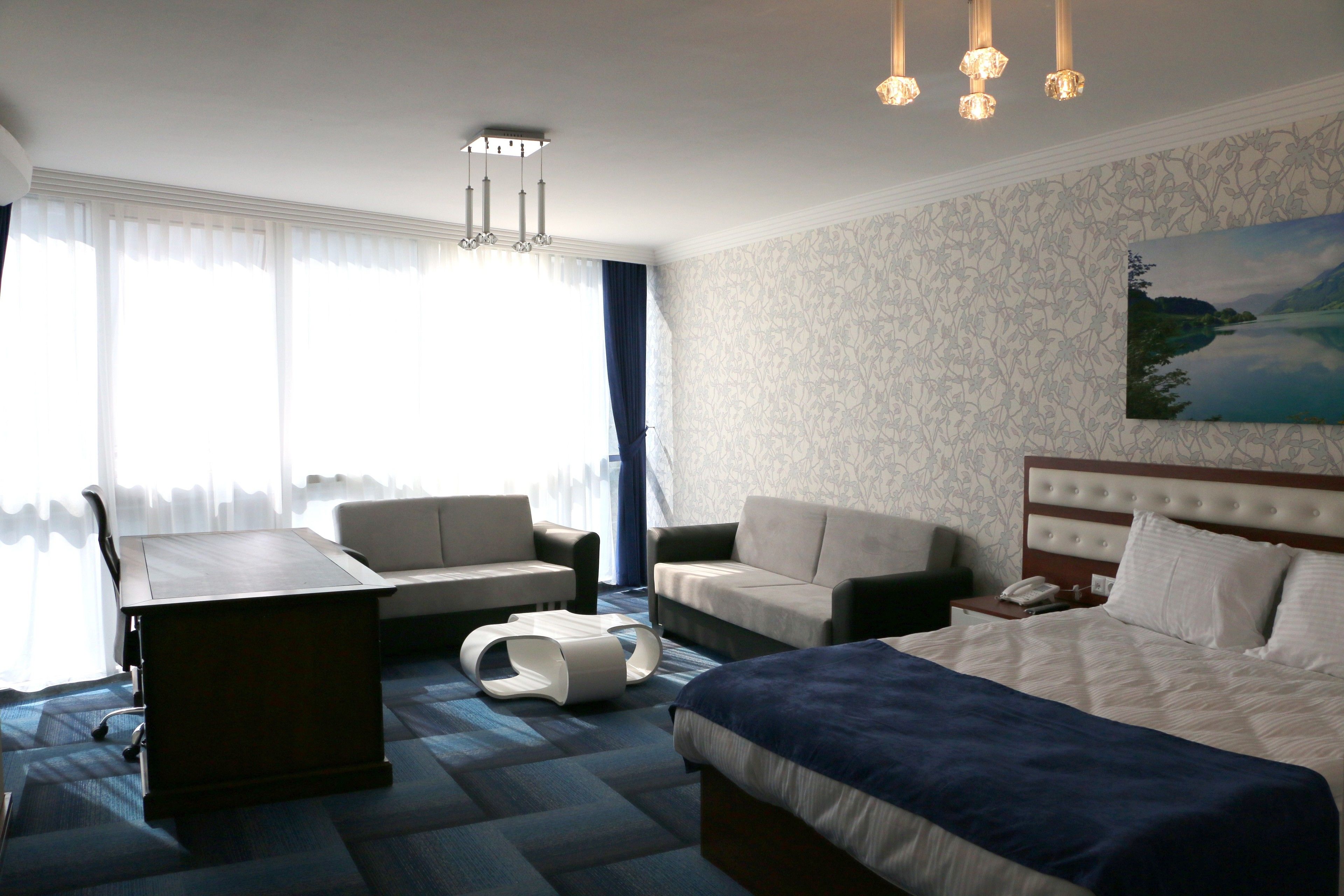 A hotel room with a bed, two sofas, a desk, and a painting on the wall.