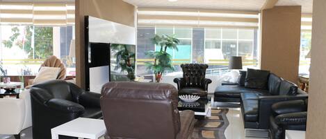 Un salón amplio con sofás de cuero, una mesa de centro blanca y un televisor de pantalla plana grande.