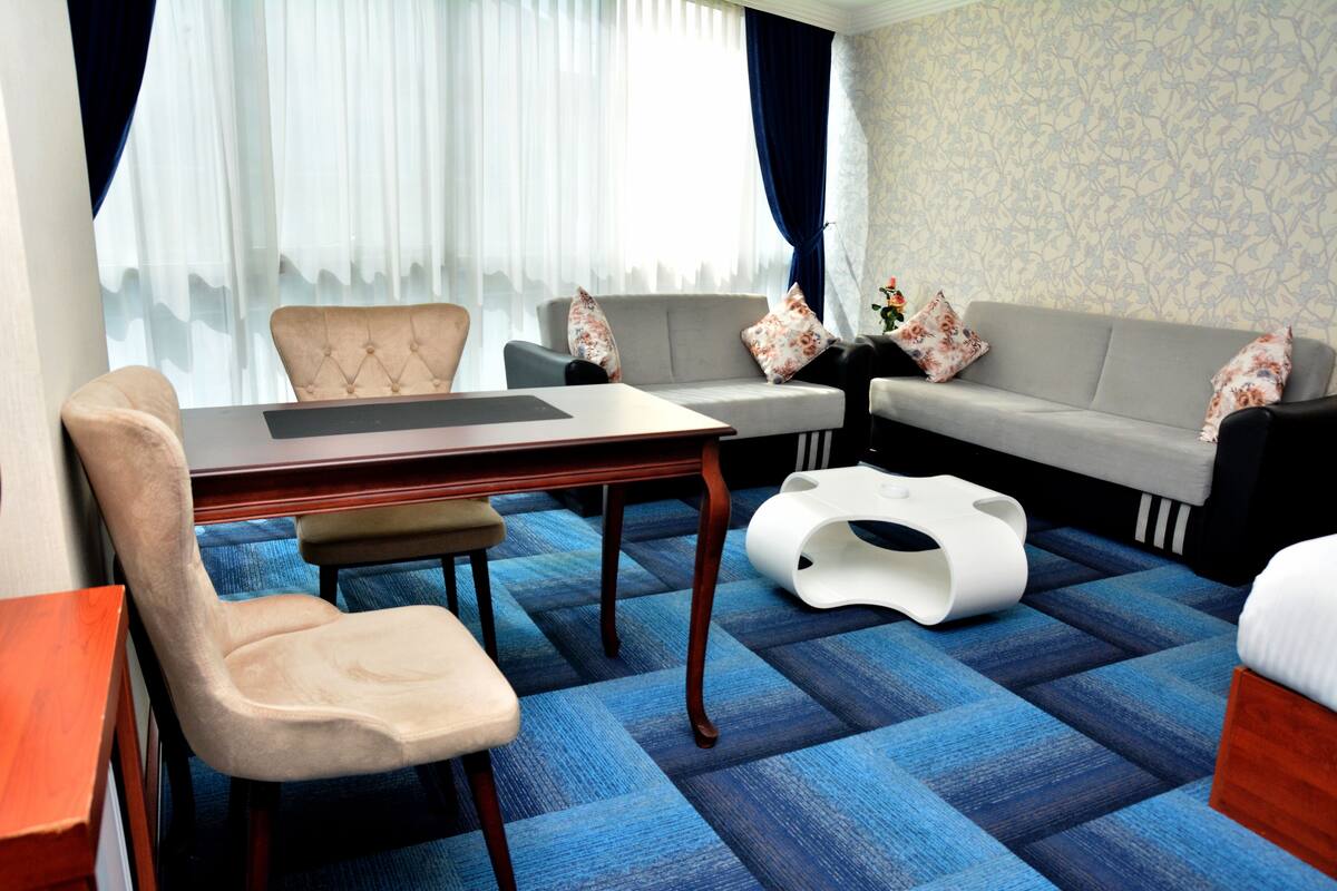 Quarto de hotel com mesa de jantar, dois sofás, uma cadeira e um objeto decorativo branco no chão.