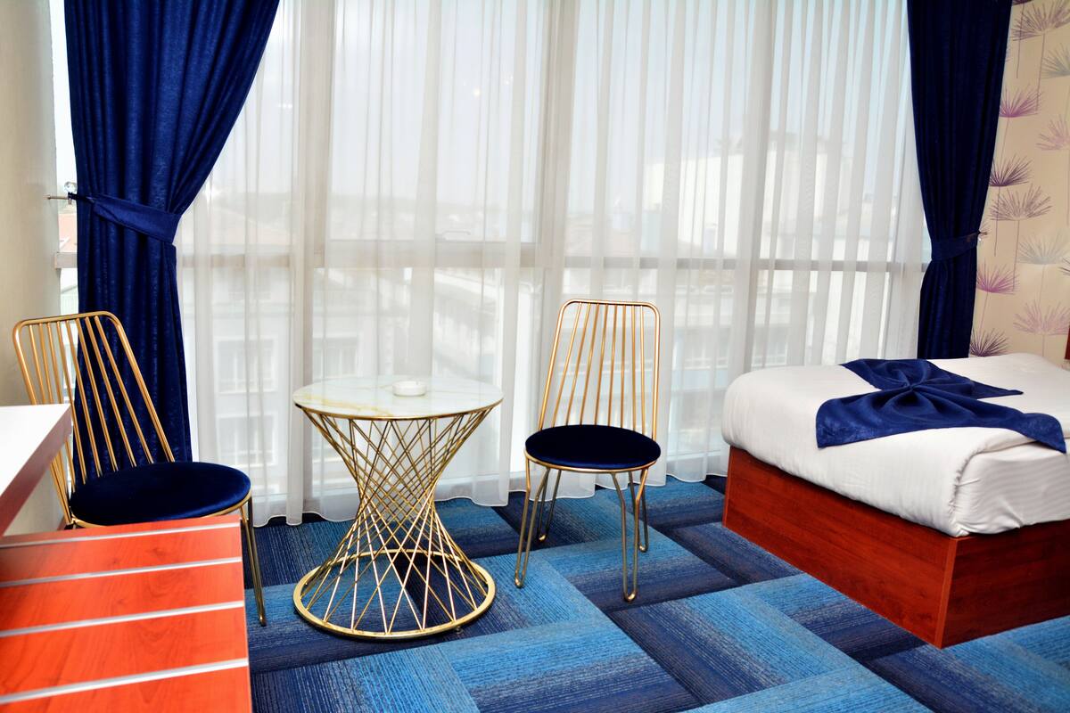 Quarto de hotel com uma cama, duas cadeiras, uma mesinha e um aparador.