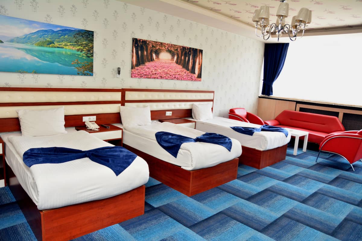 Quarto de hotel com duas camas, uma cadeira vermelha e vista para o mar.