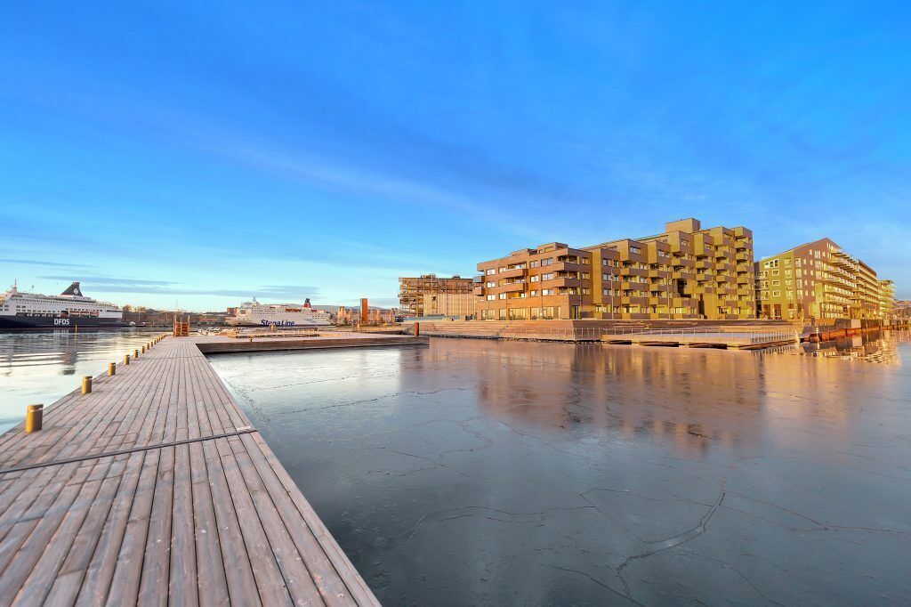 A waterfront hotel with a wooden pier extending into the water, featuring multiple balconies and a modern architectural style.