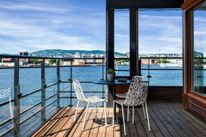 A balcony with a wooden floor, two white chairs, a small table, and a potted plant. - Wright Apartments (Oslo)