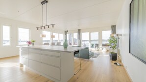 A spacious kitchen with a large island, modern pendant lights, and large windows offering a view of the city. - Wright Apartments (Oslo)