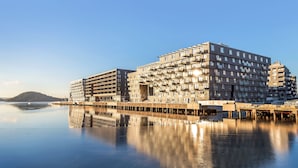 A modern multi-story building with a reflective water body in front, featuring a structured, grid-like facade and multiple balconies. - Wright Apartments (Oslo)
