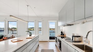 A modern kitchen with a large island, built-in appliances, and large windows offering a view of the sea. - Wright Apartments (Oslo)