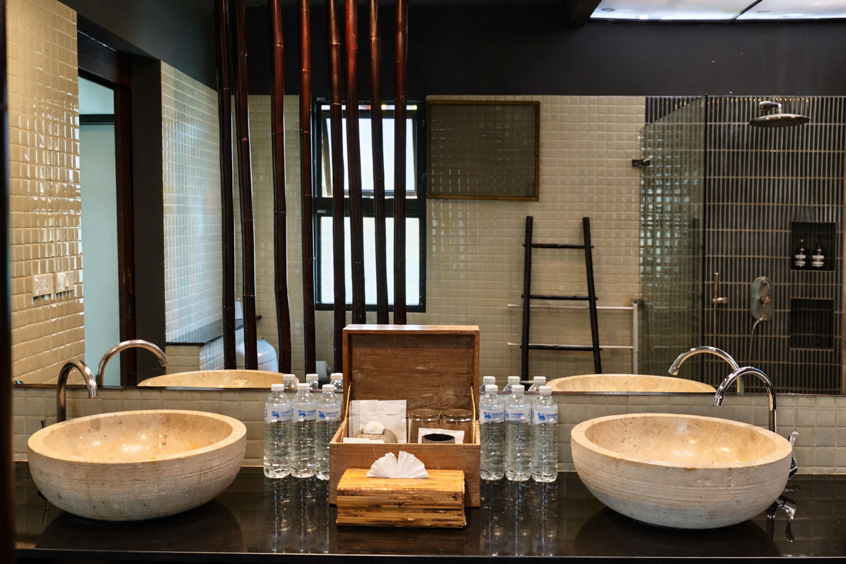 A bathroom with two large vessel sinks, a wooden box with tissues, and several water bottles.