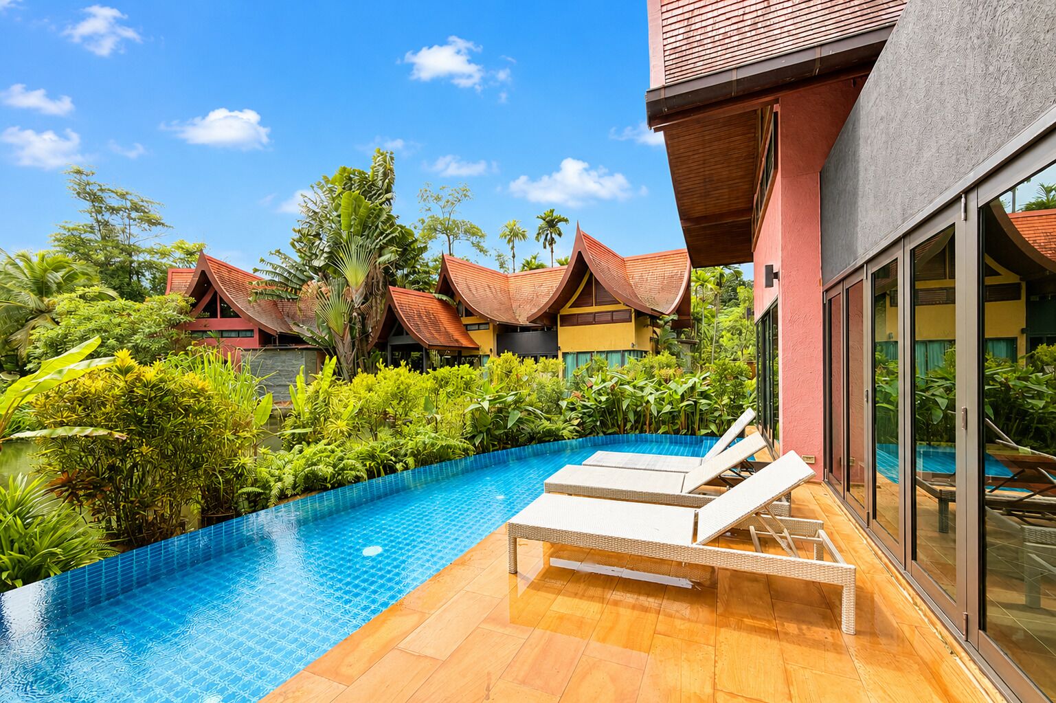 A swimming pool with lounge chairs, surrounded by lush greenery and traditional-style buildings.