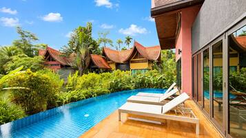 A swimming pool with lounge chairs, surrounded by lush greenery and traditional-style buildings.