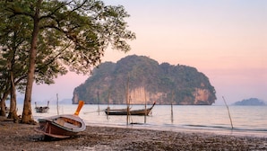 Uma praia com barcos, árvores e uma ilha ao longe.