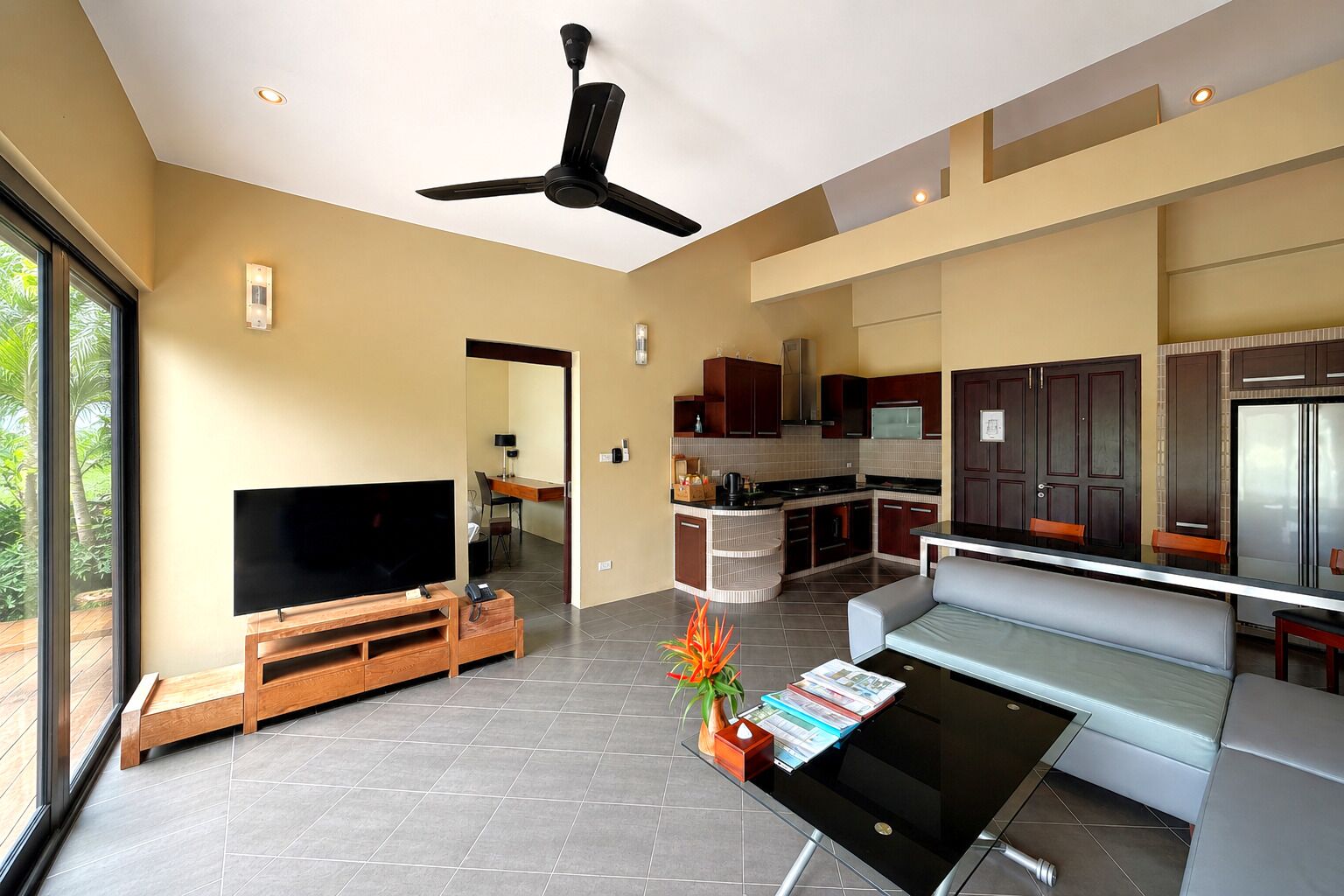 A modern kitchen with a dining area, a TV, and a ceiling fan.
