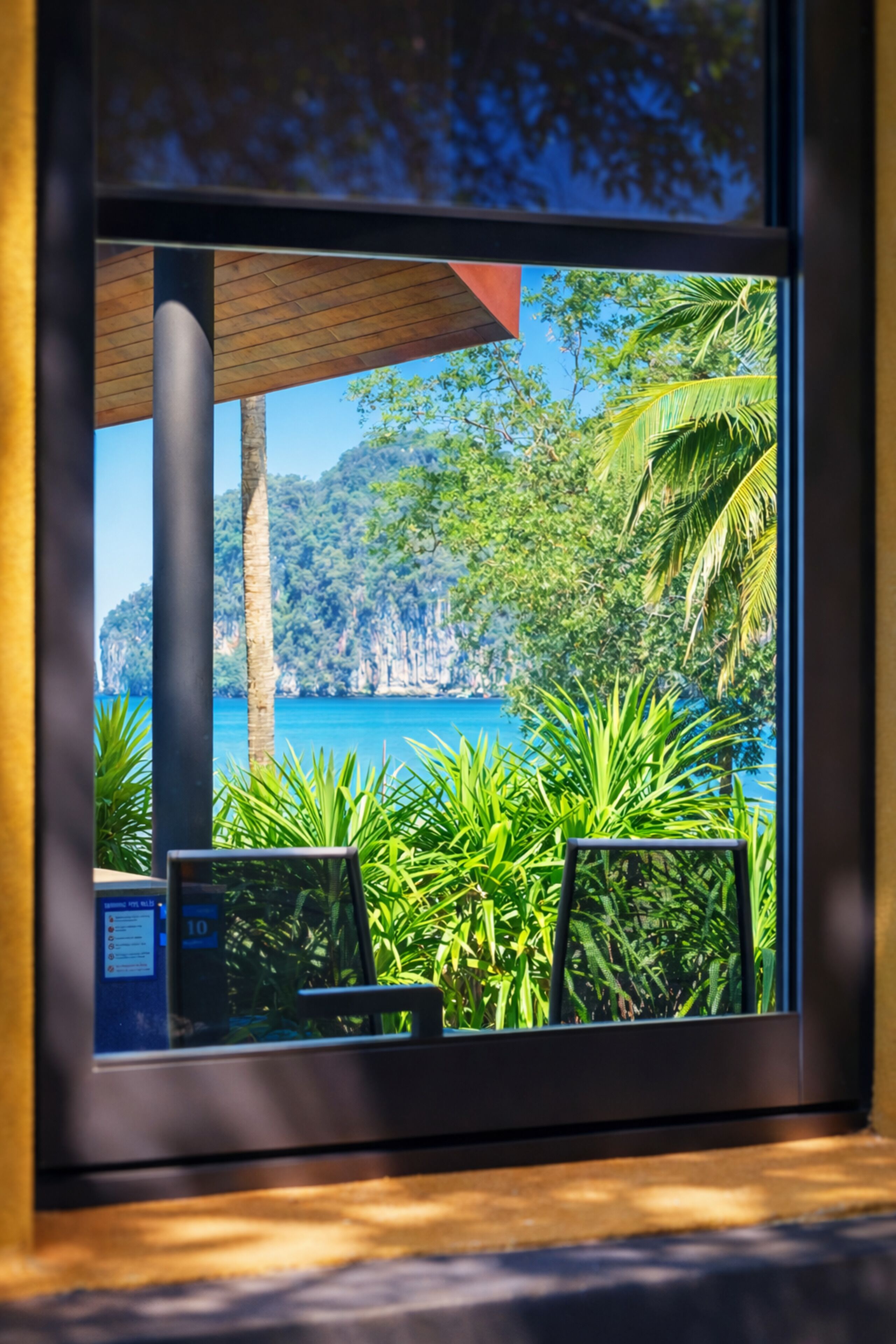 Una ventana con vistas a un paisaje tropical, que incluye vegetación y una masa de agua.