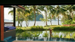 Vista de um quarto com piscina, com vista para um corpo d'água calmo, vegetação exuberante e uma montanha ao longe.