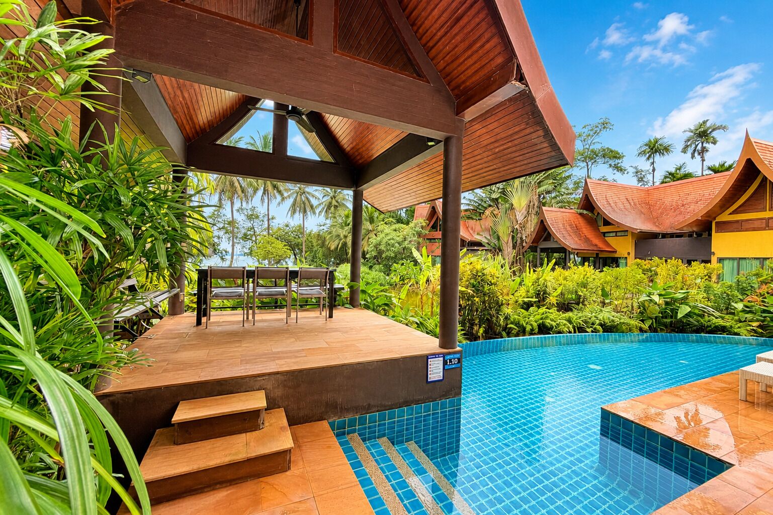 A poolside area with a wooden deck, a table with chairs, and a sign indicating a depth of 1.10 meters.