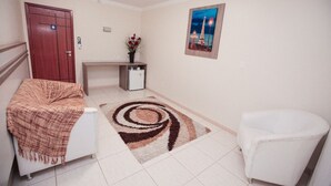 A hotel room with a white sofa, a white armchair, a small table with a vase of flowers, a painting of the Eiffel Tower, and a spiral rug. - Hotel Dom Baroni (Guarapuava)