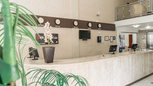 A hotel reception area with a marble counter, clocks displaying different time zones, a flat-screen TV, and a potted plant. - Hotel Dom Baroni (Guarapuava)