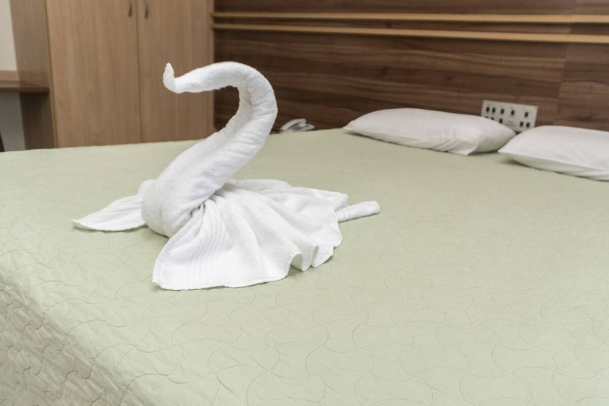 Una cama con una escultura de toalla con forma de cisne, un cabecero de madera y dos almohadas.