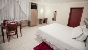 A bedroom with a bed, a desk, a chair, a wardrobe, a mirror, and a door. - Hotel Dom Baroni (Guarapuava)
