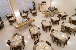Een ruime eethoek met meerdere ronde tafels, elk voorzien van borden, bestek en glazen.
