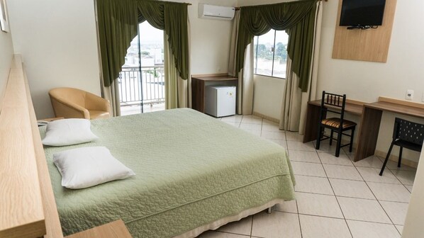 Una habitación de hotel con cama, escritorio, silla, televisor y ventana con cortinas.