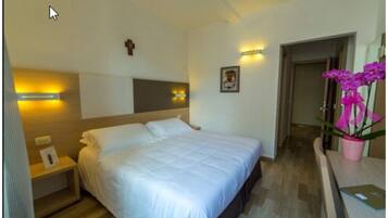 Habitación de hotel con una cama grande, mesitas de noche, una lámpara de pared, un cuadro enmarcado y una planta en maceta.