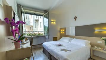 Une chambre d’hôtel avec un grand lit, un bureau avec une chaise, une fenêtre donnant sur des immeubles et un plateau avec des articles pour le petit-déjeuner.
