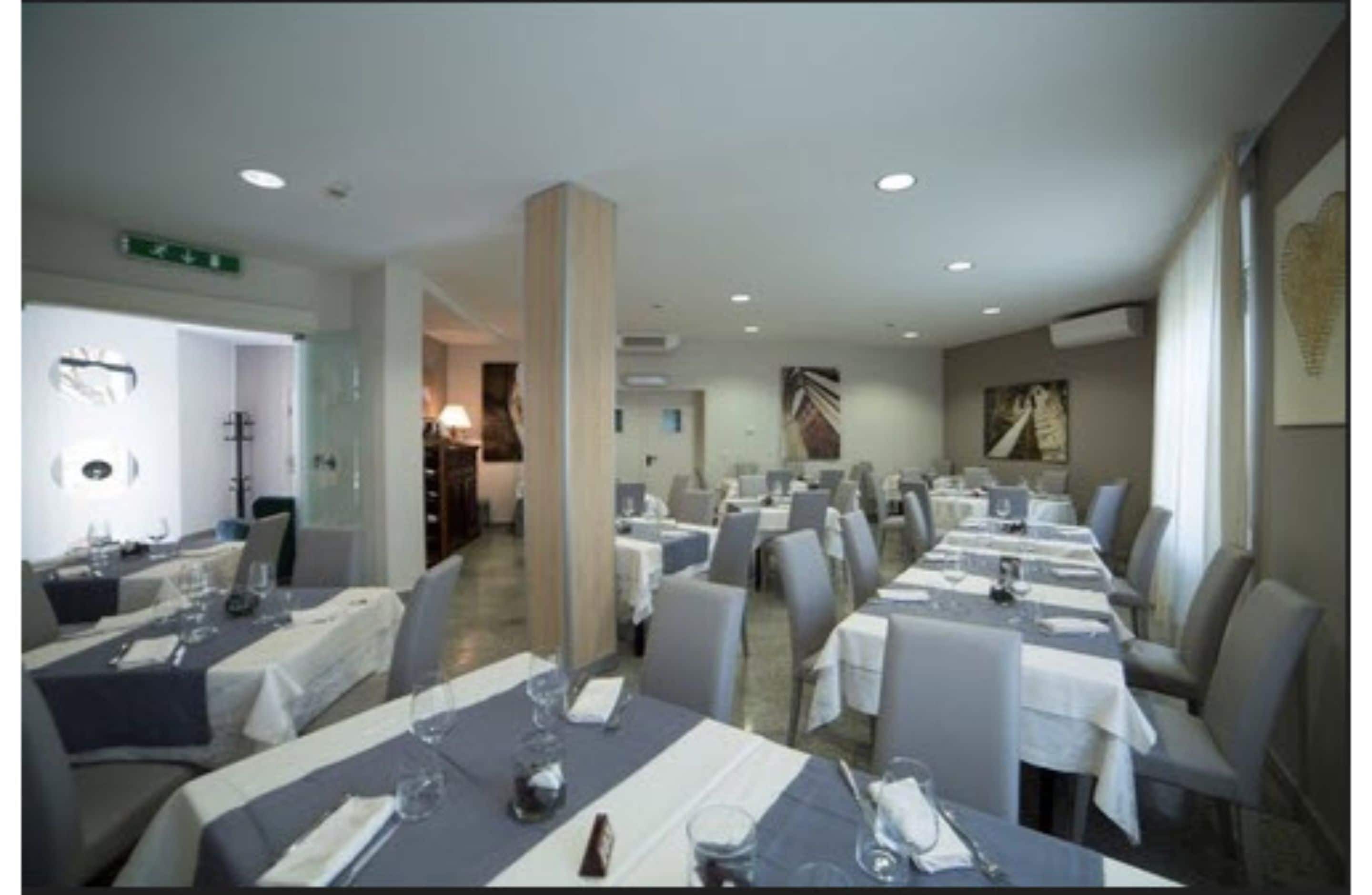 Un área de comedor con varias mesas dispuestas para el servicio, un pilar en el centro y vistas del comedor a través de un separador de vidrio.