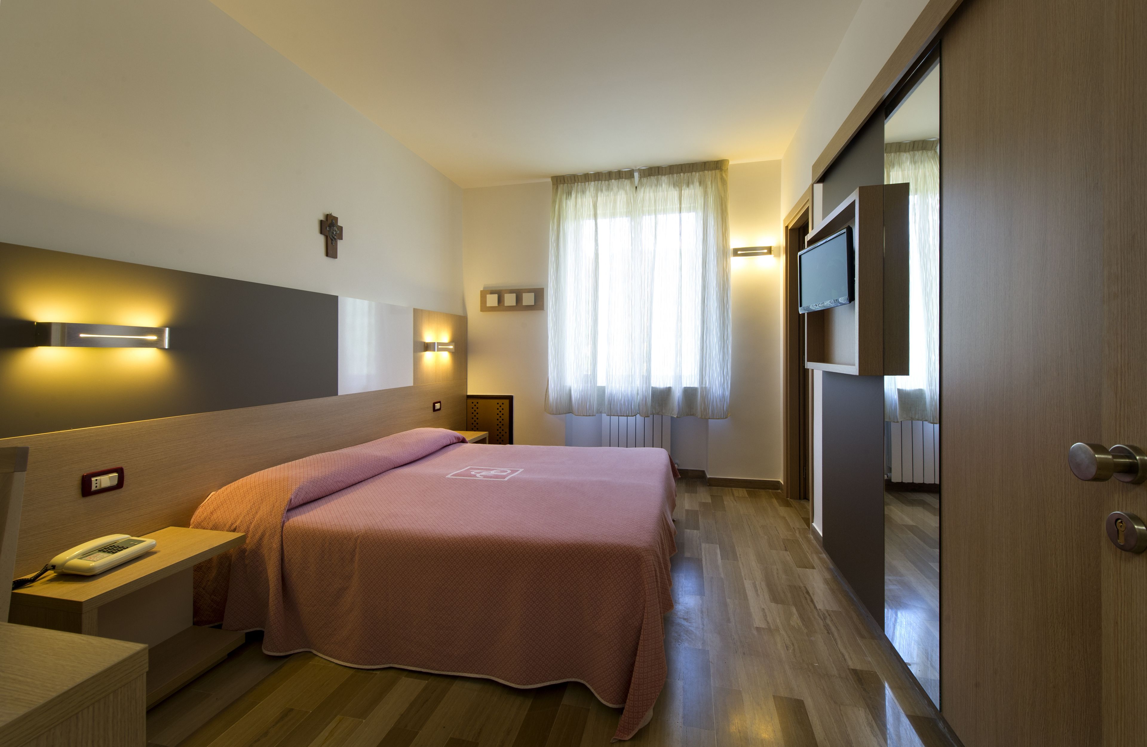 Une chambre d’hôtel équipée d’un lit, d’une table de chevet, d’une lampe et d’un téléviseur fixé au mur.