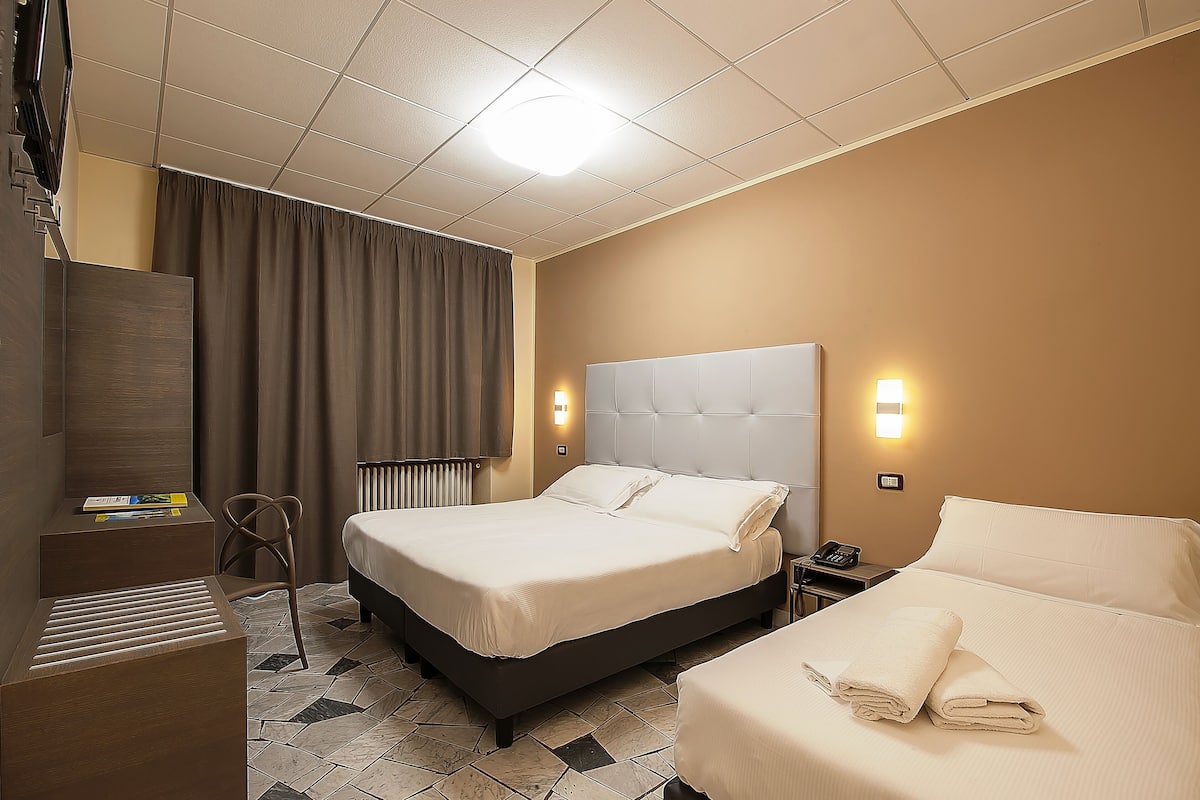 A hotel room with a large bed, a smaller bed, a desk, a chair, and a radiator.