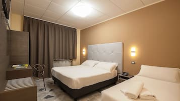 A hotel room with a large bed, a smaller bed, a desk, a chair, and a radiator.