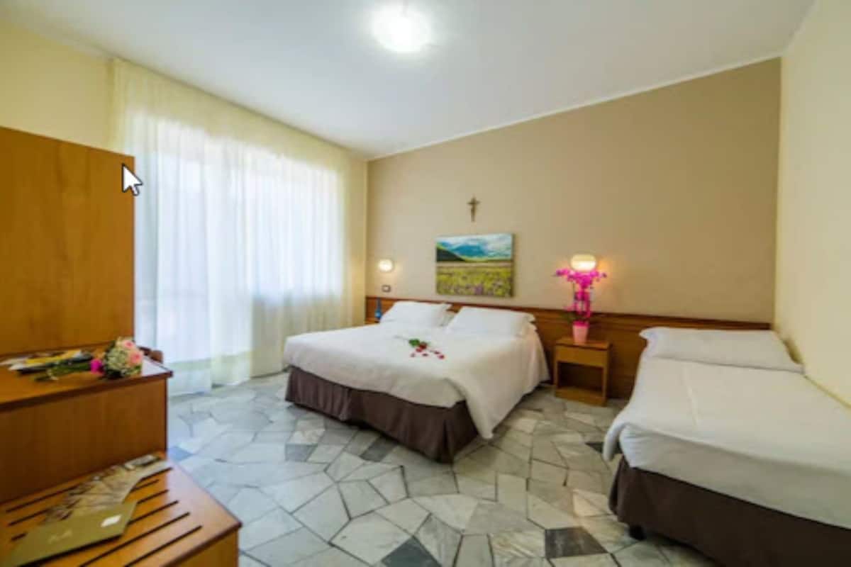 A hotel room with a bed, a wooden desk, a nightstand, and a painting on the wall.