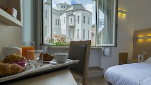 Habitación de hotel con una mesa de comedor dispuesta para el desayuno, una cama y vistas a un edificio histórico a través de la ventana.