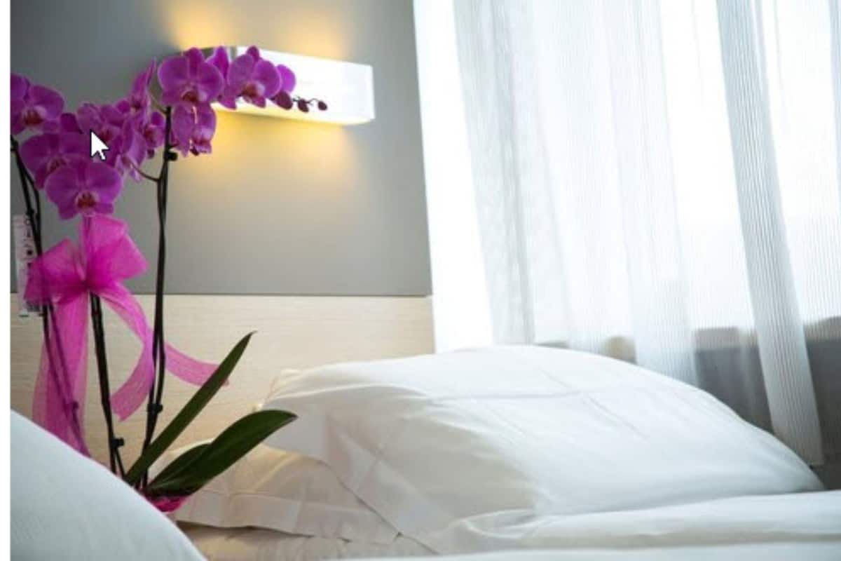 A hotel room with a bed, white pillows, and a wall-mounted light fixture.