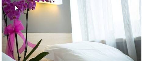 Una habitación de hotel con cama, almohadas blancas y una lámpara fijada a la pared.