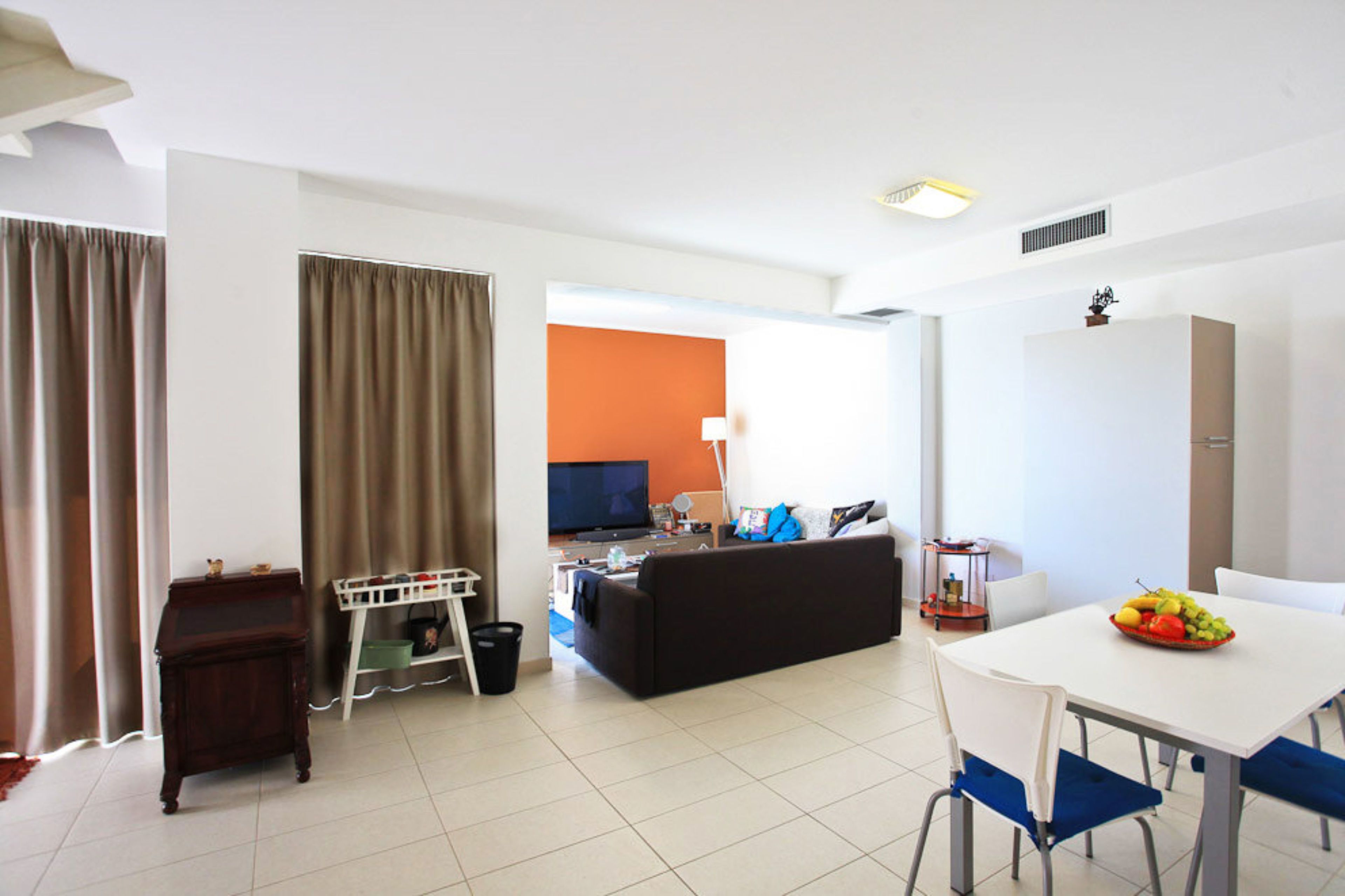 A modern living room with a sofa, dining table, and a television in the background.