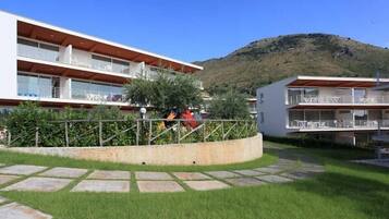 A modern two-story building with balconies, surrounded by a landscaped garden with stone pathways and greenery.