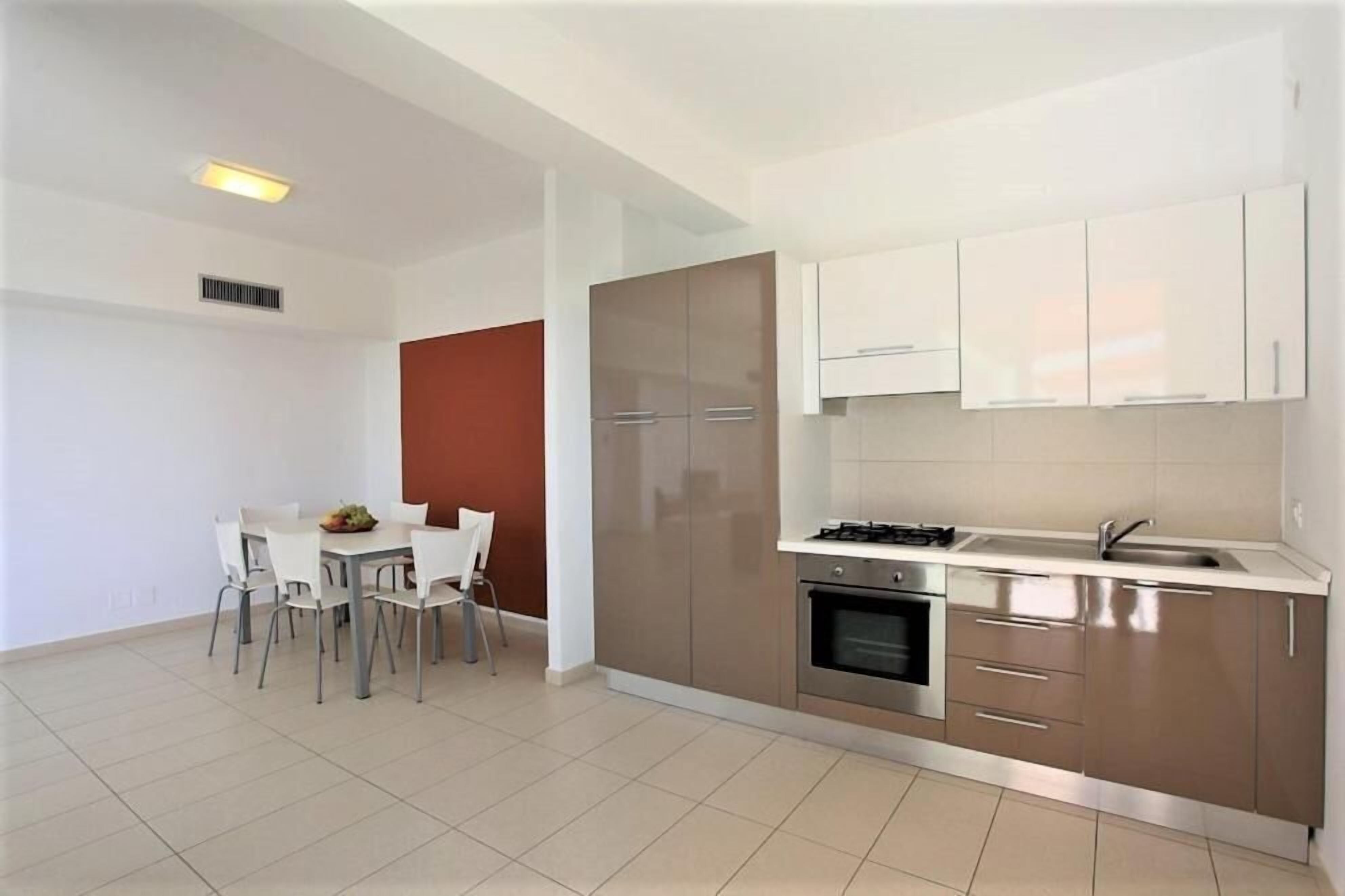 Una cocina moderna con armarios blancos, una estufa a gas y un lavamanos. Hay una zona de comedor con una mesa y sillas.
