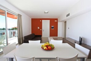 Moderni hotellihuone, jossa on ruokailutila, sohva ja hedelmäkulho pöydällä.