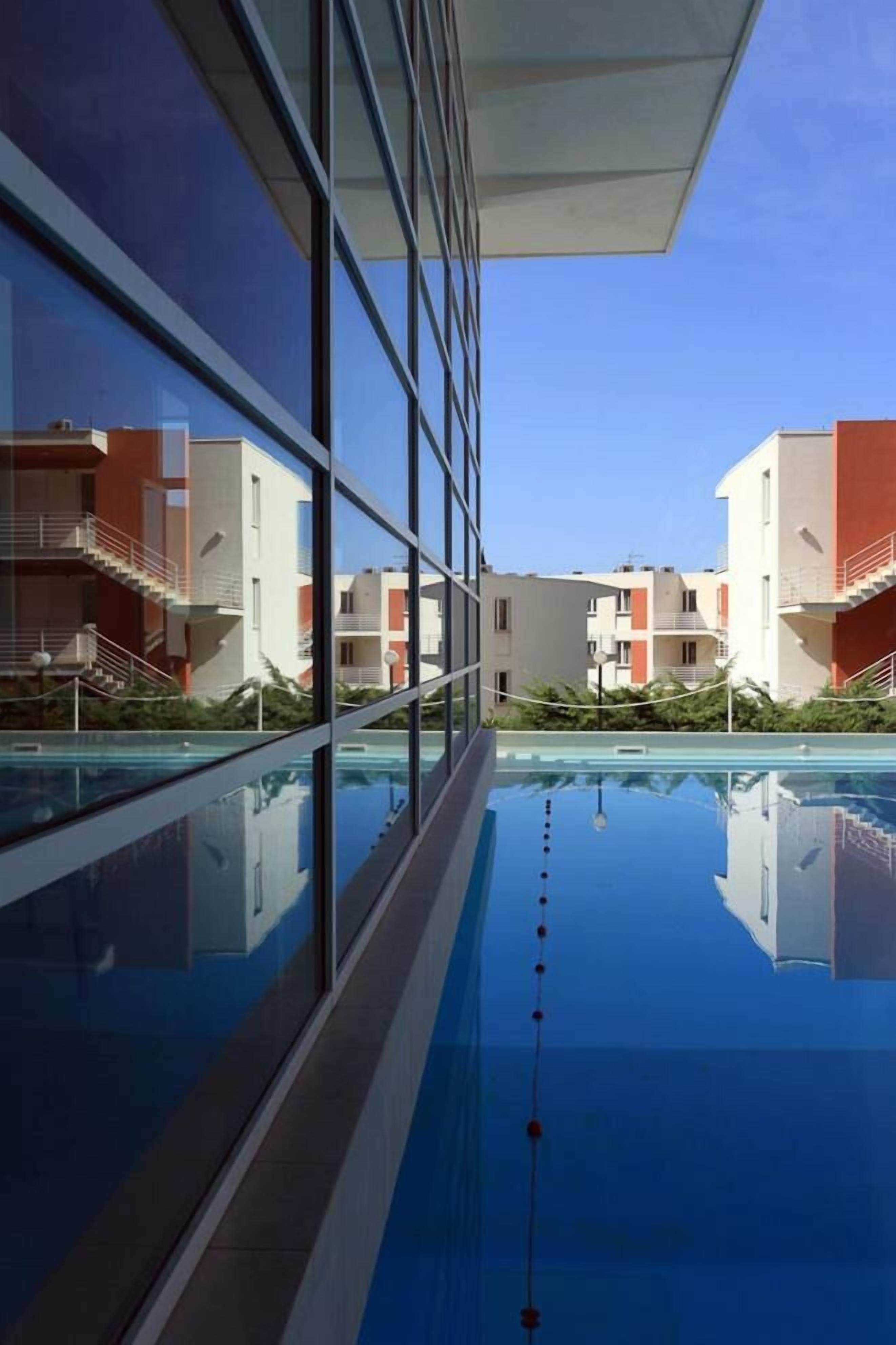 A modern building with a reflective pool, large windows, and balconies.