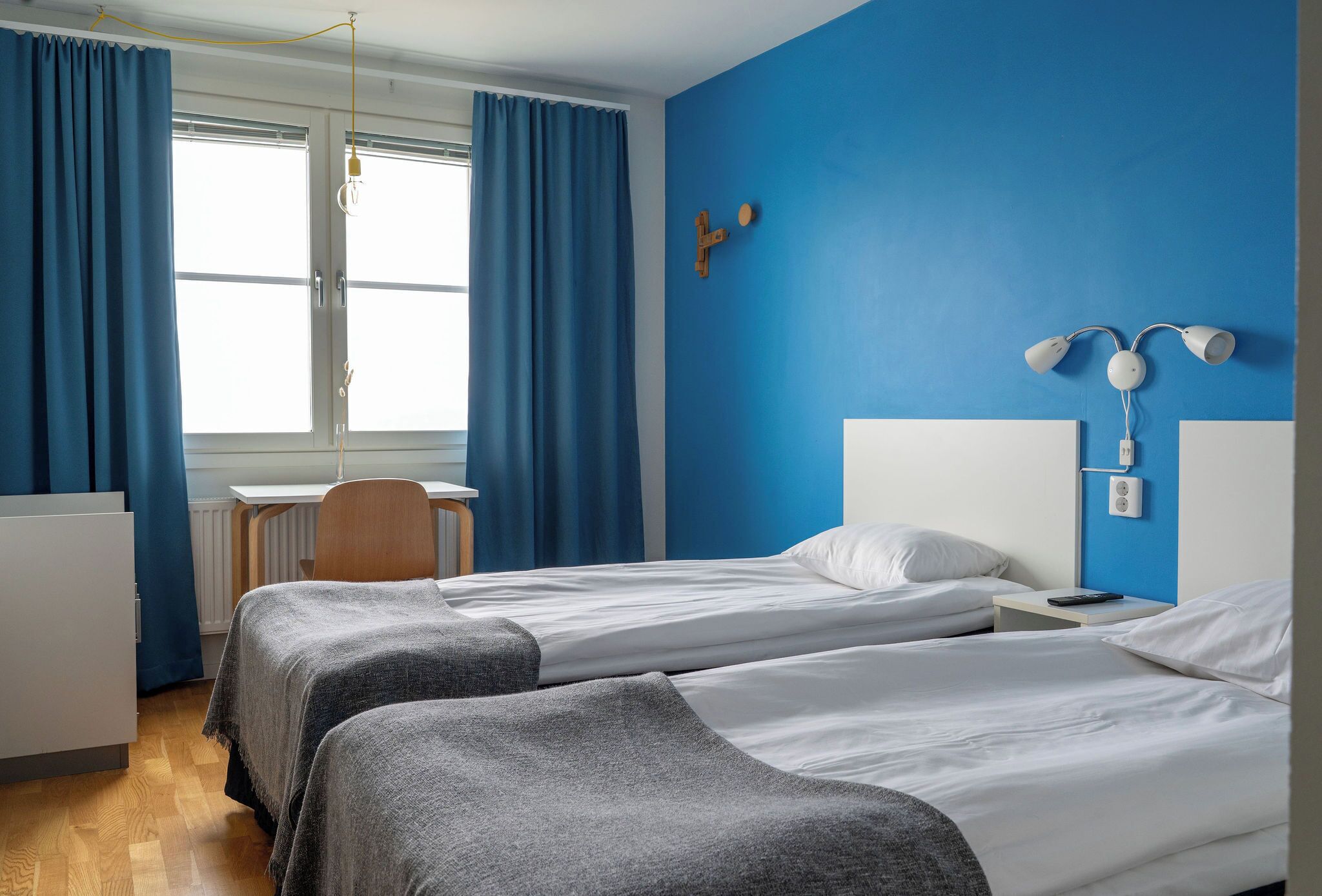 Een hotelkamer met twee bedden, een bureau, een stoel en een raam met gordijnen.