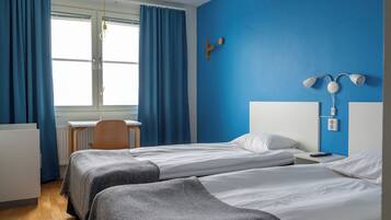 Een hotelkamer met twee bedden, een bureau, een stoel en een raam met gordijnen.