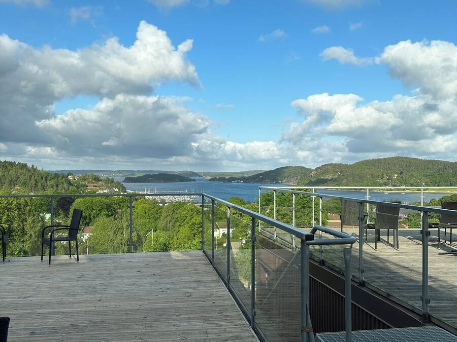 Una terraza de madera con barandillas metálicas que da vista a una masa de agua y un paisaje distante.