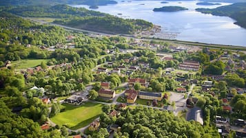 An aerial view of a town with a mix of residential and commercial buildings, surrounded by lush greenery and a large body of water.